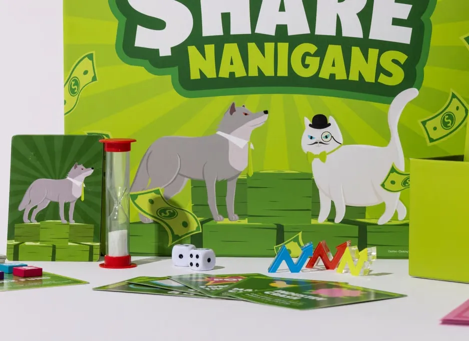 The Sharenanigans game in play in front of its box art: the wolf and the fat cat, share blocks, dice, a sand timer and cards